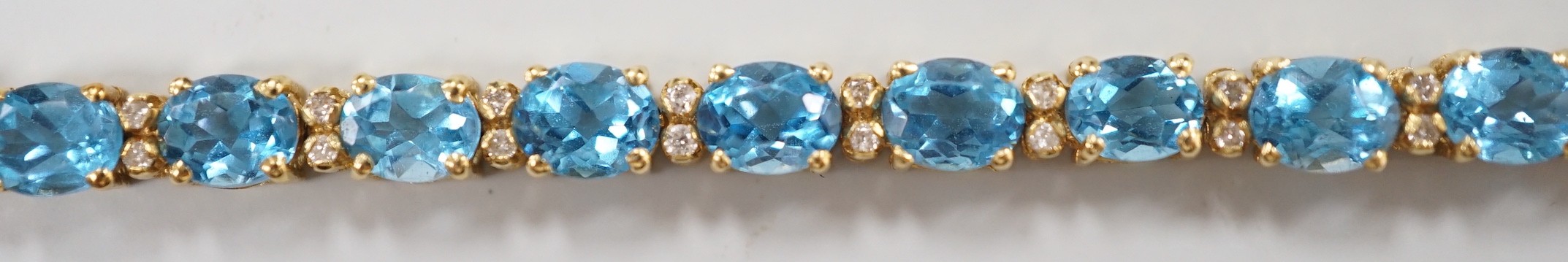 A modern 750 yellow metal and blue topaz set line bracelet, with diamond chip spacers, 17.75cm